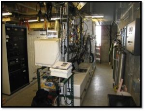 Photo of a research lab showing gas cylinders, controller racks, storage boxes, cables and a laptop.