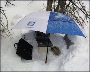 Laptop on snowy ground, protected by an umbrella.